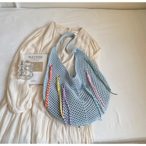 Detail of light blue crochet tote bag with colorful braided tassels on white dress