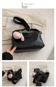 Detail view of black leather tote bag with wide strap and peach plush pendant