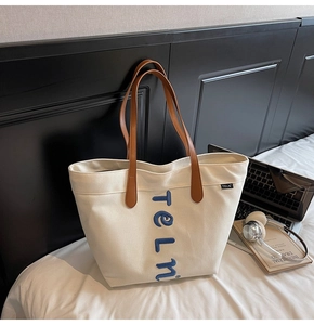 Close-up of cream canvas tote bag with blue towel embroidery letter and brown leather handles