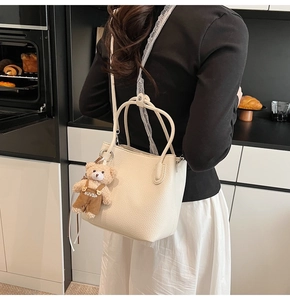 Detail of cream bucket bag in lychee leather texture with a cute small bear charm