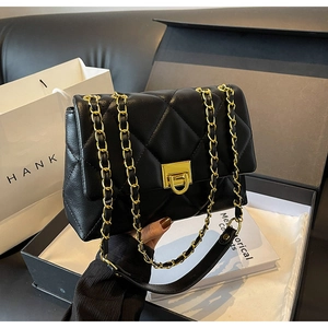 Détail d'un sac bandoulière en cuir matelassé noir avec chaîne dorée et fermoir carré