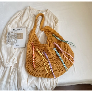 Close-up of ginger yellow crochet tote bag with colorful spiral woven pendants on white dress