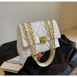 Détail d'un sac matelassé blanc avec chaîne dorée posé sur une veste en cuir