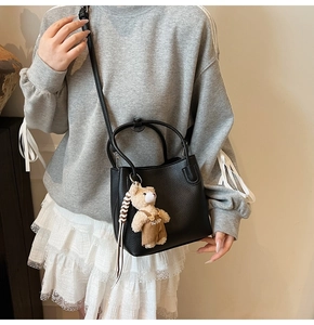 Detail of black pebbled leather bucket bag with cute plush bear charm on strap