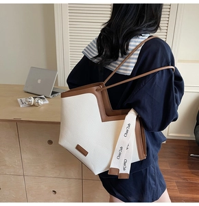 Detailed side view of a large tote bag with contrast brown trim and stylish branding strap