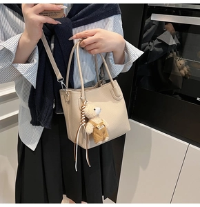 Detail showing beige bucket bag with lychee texture leather and plush bear charm