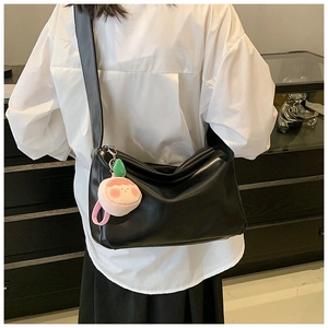 Detail of black glossy leather tote bag with wide strap and pink plush charm accessory