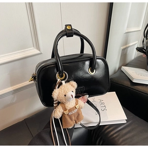 Detail view of black patent leather handbag with a cute teddy bear charm accessory