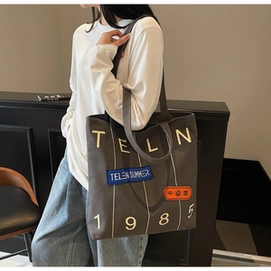 Detailed view of dark grey canvas tote bag with TELN 1985 text and vintage patches