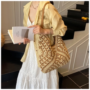 Close-up of woven straw tote bag with brown leather straps shown on a female model