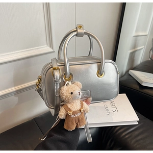 Detail of silver metallic Boston bag with adjustable strap and cute teddy bear charm
