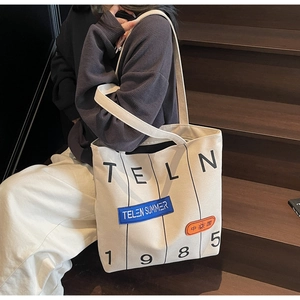Detailed close-up of a beige canvas tote bag with letter prints and decorative patches