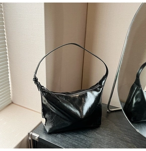 Detail of black semi-circle hobo bag with glossy finish and silver heart charm pendant