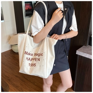 Detail of a large off-white canvas tote bag featuring brown letter print on a model