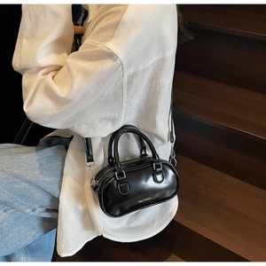 Detail of a shiny black mini Boston bag styled on a model with metallic hardware accents