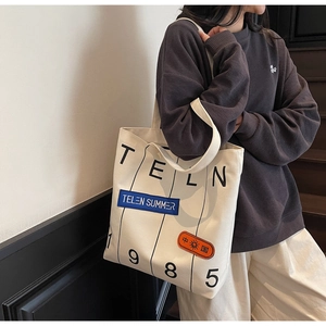 Detail of canvas tote bag showing TELN 1985 print and colorful decorative patches