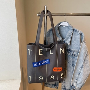 Detail of grey canvas tote bag with white TELN 1985 lettering and decorative patches