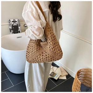 Detailed back view of a woman wearing the woven straw tote bag with brown leather strap