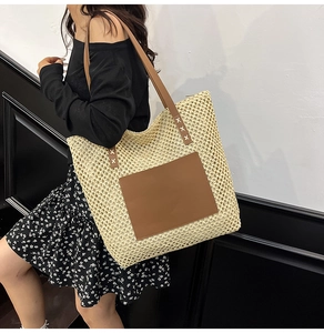 Detail view of woven straw tote bag with brown leather pocket and dual shoulder straps