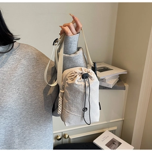 Détail d'un sac bandoulière crème avec fermeture à cordon et pendentif tressé