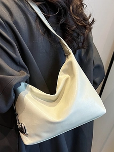 Minimalist beige underarm bag in sleek faux leather shown on shoulder with grey coat
