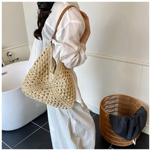 Close-up of a large beige straw tote bag with brown leather straps held by a model