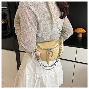 Detail of light yellow quilted saddle bag with dual chains and woven charm accessory