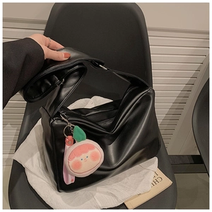 Detail of minimalist black PU tote bag with wide strap and cartoon plush charm