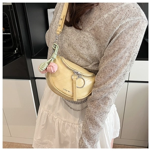 Detail of yellow quilted half-moon crossbody bag with decorative woven charms on the strap