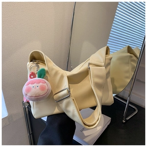 Detail of creamy yellow PU tote bag with wide strap and pink peach plush pendant charm