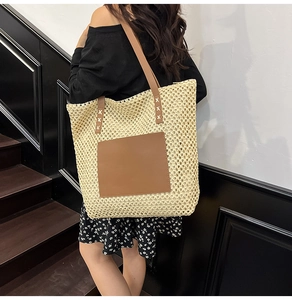 Large straw tote bag with brown leather straps shown on model in a minimalist setting