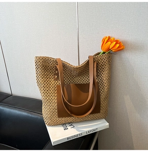 Close-up of a large straw tote bag with a dark brown leather pocket and long handles