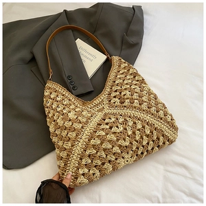 Detail of woven straw tote bag featuring contrast colors and brown leather shoulder straps