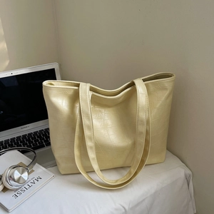 Detail of creamy yellow tote bag with crocodile texture on a desk with laptop