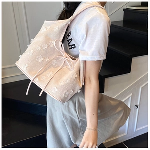 Detail of a beige tote bag with white 3D petal decorations and side drawstring bow
