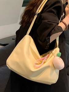 Minimalist cream yellow wide strap tote bag with peach plush charm shown on model