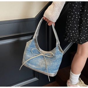 Dettaglio della texture in denim azzurro e del fiocco in metallo lucido sulla borsa a mano