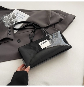 Detailansicht der schwarzen Lackleder-Achseltasche mit weißem Logo auf grauem Blazer