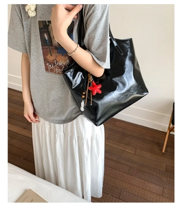 Détail d'un sac cabas en cuir verni noir avec charms étoiles porté par un mannequin de côté