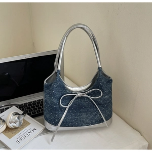 Dettaglio della borsa in denim con fiocco argento e finiture metalliche su scrivania bianca