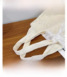 Detail shot of the cream white floral lace texture and reinforced handles on a canvas tote bag