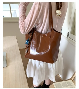 Détail du sac cabas en cuir verni marron foncé avec pendentif étoile porté par un modèle