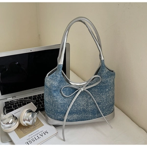 Dettaglio borsa hobo in denim blu con grande fiocco argento su scrivania con gadget