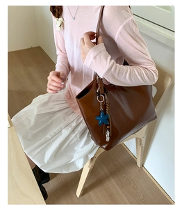 Sac fourre-tout en cuir marron avec breloque étoile bleue porté par un mannequin en décor
