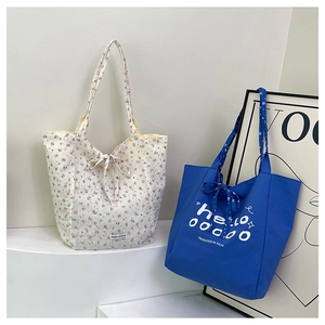 Détail des sacs cabas en toile à fleurs et bleu avec des nœuds décoratifs sur fond blanc