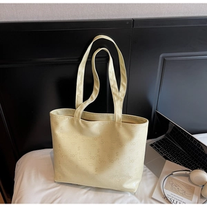 Detailed close-up of cream PU leather tote bag with embossed letters on a white bed