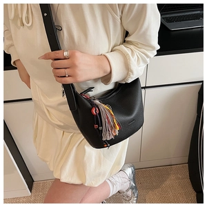 Détail du sac à main noir en cuir grainé avec pompon bohème porté par le mannequin