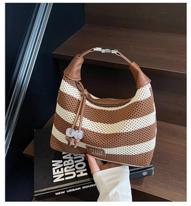 Detail of striped woven shoulder bag with brown faux leather strap and beaded charm on wood
