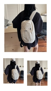 Detailed view of the wrinkled nylon texture and brand tag on this minimalist cream backpack