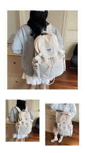 Détail du sac à dos en toile beige avec fermeture à rabat et écusson noir tissé de la marque